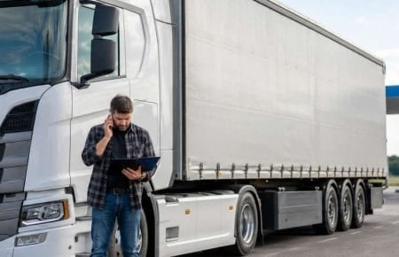 Șofer coordonând un transport lângă o semiremorcă cu prelată albă